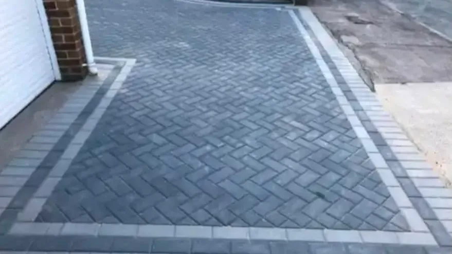 Charcoal block paving laid in herringbone, with a pale kerb line around the edge